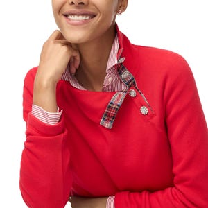 Red sweatshirt with a plaid tartan collar and jeweled buttons, over a red and white striped shirt.