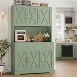 A kitchen features sage green cabinets with X-patterned doors, brass handles, and a countertop displaying an air fryer, cutting boards, and decor items. A corner section includes a black oven, white toaster, and shelves with jars and plants.