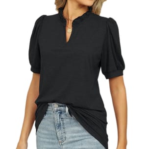 A woman is wearing a black blouse with puff sleeves and a ruffled neckline, paired with light blue jeans. She accessorizes with a circular pendant necklace.