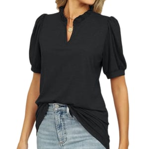 A woman is wearing a black blouse with puff sleeves and a ruffled neckline, paired with light blue jeans. She accessorizes with a circular pendant necklace.