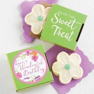 Two flower-shaped cookies with white icing and a green center, presented in green boxes with messages: \“Enjoy This Sweet Treat\“ and \“have a Wonderful Birthday\“ with floral designs.