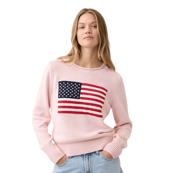 A person wears a light pink sweater with an American flag design on the front, paired with light blue jeans.