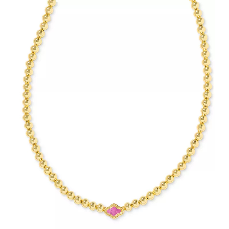 A gold bead necklace featuring a central pink stone with a decorative gold border.