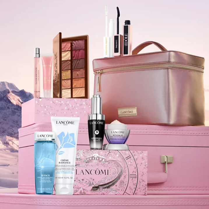 A Lancôme beauty set displayed with skincare products, makeup items like mascara and an eye palette, and a shimmering pink travel case, all placed against a snowy mountain backdrop.