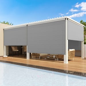 A gray roller sun shade is partially closed around a pergola on a wooden deck by a pool, providing shade and privacy with a modern design. Wicker chairs and a table are visible inside the shaded area.