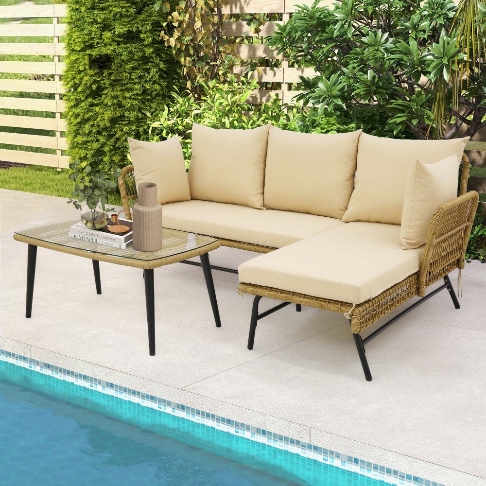 Outdoor sectional sofa set with beige cushions, accompanied by a glass-top table holding decorative items, situated near a pool with surrounding plants and fencing.