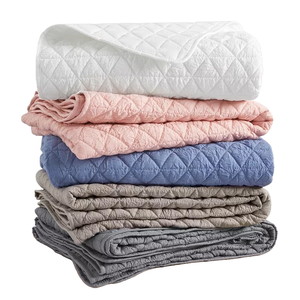 A stack of quilted blankets in white, pink, blue, beige, and gray colors, featuring a diamond pattern.