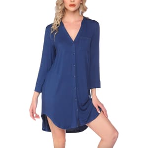 A woman is wearing a blue, long-sleeved button-up shirt dress with a V-neck and chest pocket. The dress features a slight high-low hem.