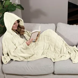 A person relaxes on a couch wearing a hooded blanket while reading a book. The blanket has a quilted design and covers the entire body.