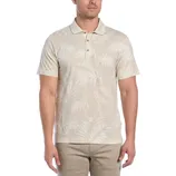 A light beige polo shirt with a tonal palm tree pattern, short sleeves, and a buttoned collar, paired with beige pants.
