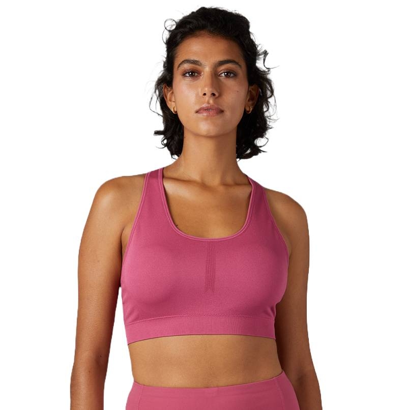 A person wearing a pink sports bra with a scoop neck and racerback design. They have short, curly black hair and are also wearing matching pink leggings.