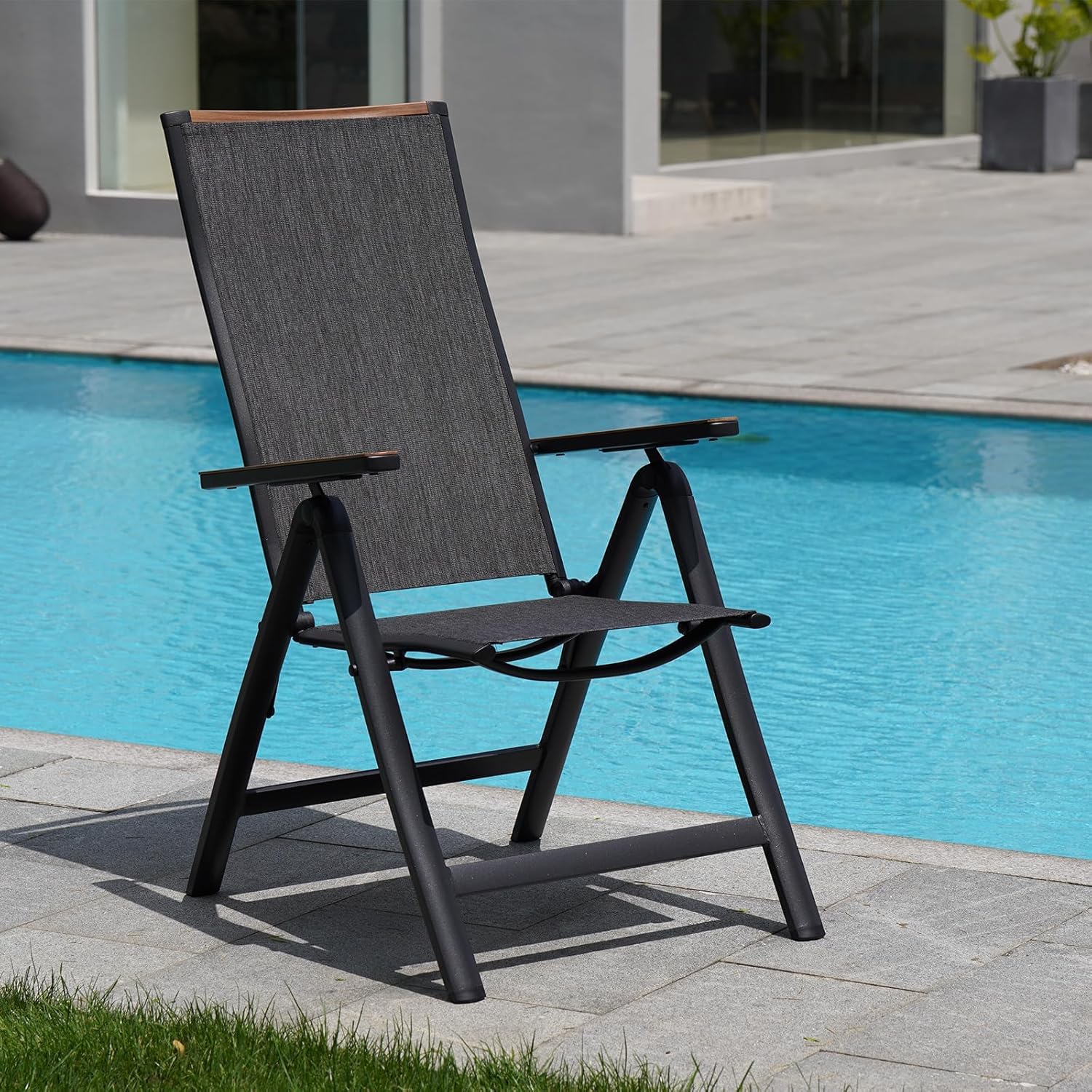 A black outdoor lounge chair with a fabric backrest and seat, beside a swimming pool.