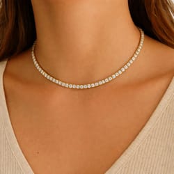 A gold choker necklace with sparkling round diamonds encircles the neck, worn over a light beige top.