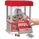A miniature claw machine filled with assorted candies, featuring a red and silver design and joystick controls. It is accompanied by a collection of tokens for operation.