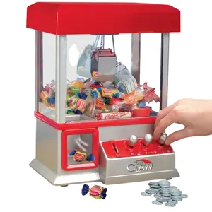 A miniature claw machine filled with assorted candies, featuring a red and silver design and joystick controls. It is accompanied by a collection of tokens for operation.