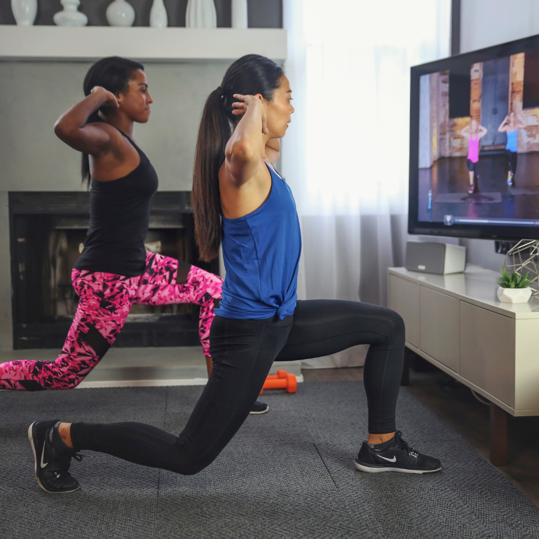 Two people are engaging in a lunge exercise following an instructor on a TV, which is part of a home workout program subscription service.