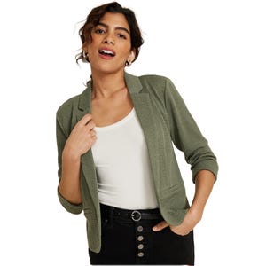A woman is wearing a textured olive green cropped blazer with three-quarter rolled sleeves and notched lapels, over a white tank top and black high-waisted jeans with button detailing.
