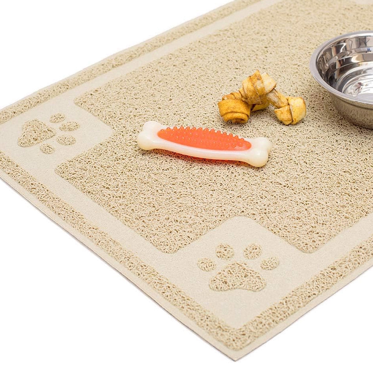 A beige pet food mat with a raised border, paw print decorations, a stainless steel bowl, a bone-shaped rubber toy, and two twisted dog treats.