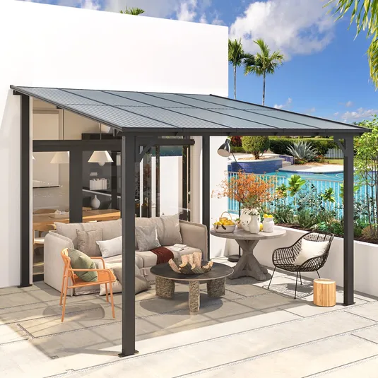 A modern outdoor patio with a metal-framed canopy, featuring seating including a sofa with pillows, a wicker chair, and a wooden armchair, surrounding a stone coffee table. A side table holds decorative vases, and a pool is visible in the background.