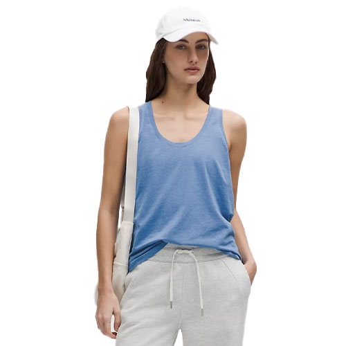 A woman is wearing a blue tank top, gray sweatpants, and a white cap. She has a white bag over her shoulder.
