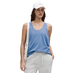 A woman is wearing a blue tank top, gray sweatpants, and a white cap. She has a white bag over her shoulder.