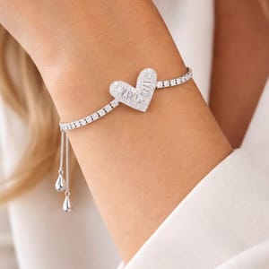 A silver bracelet features a heart-shaped pendant with baguette and round-cut stones, accompanied by an adjustable chain and teardrop-shaped ends.