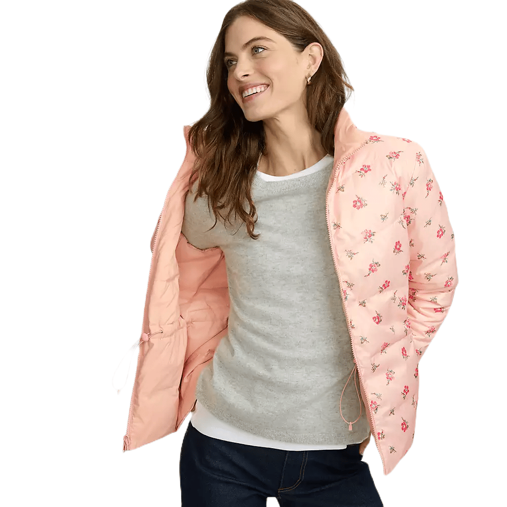 A woman is wearing a light pink floral quilted jacket over a grey sweater, paired with dark jeans.