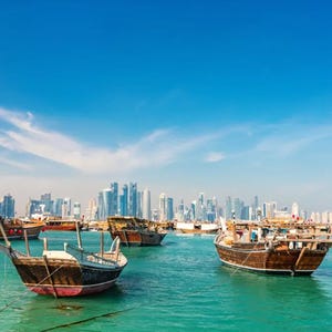 Traditional wooden boats in a turquoise sea with a modern city skyline in the background.