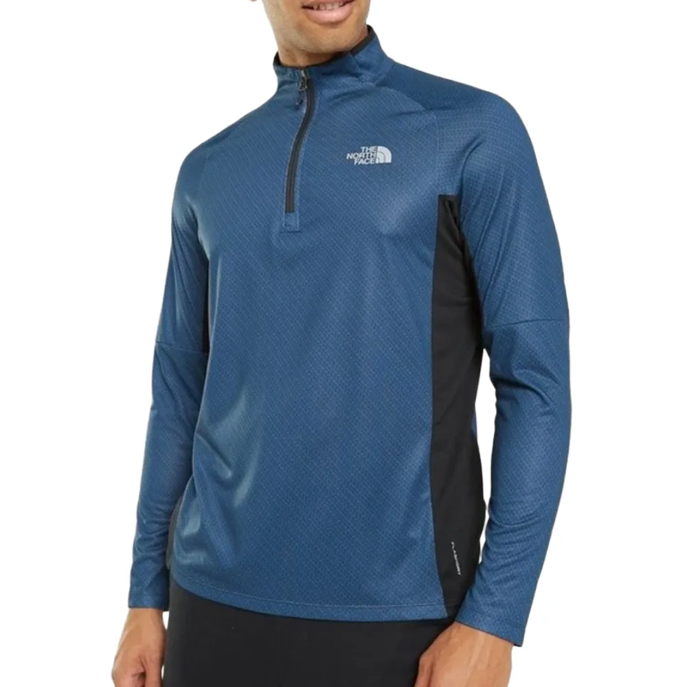 A man is wearing a blue, long-sleeve, quarter-zip athletic top with \“The North Face\“ logo on the chest.