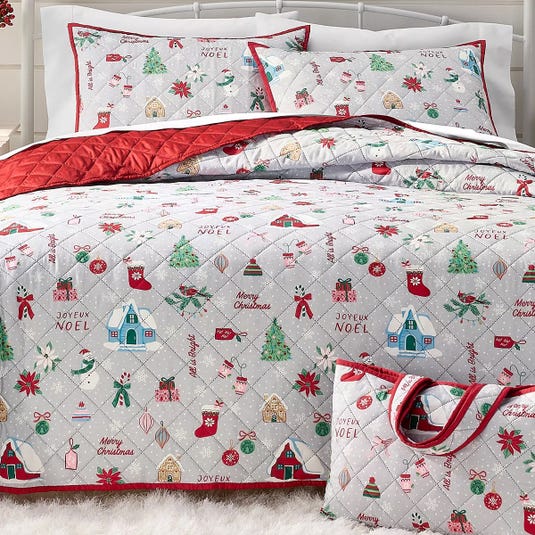 A festive bedding set featuring Christmas-themed designs with trees, stockings, and holiday phrases like \“Joyeux Noel\“ and \“Merry Christmas,\“ in red, green, and white colors. The set includes a quilt, pillowcases, and a matching bag.