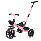A pink tricycle with black accents features a rear handlebar for adult steering assistance, front basket, and a rear storage compartment.