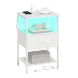 White modern nightstand with a glowing shelf, featuring a wireless charging pad, a mug, and headphones on books. It includes a drawer, a bottom shelf with a box, and power outlets with a cable.