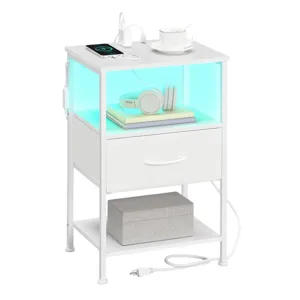 White modern nightstand with a glowing shelf, featuring a wireless charging pad, a mug, and headphones on books. It includes a drawer, a bottom shelf with a box, and power outlets with a cable.