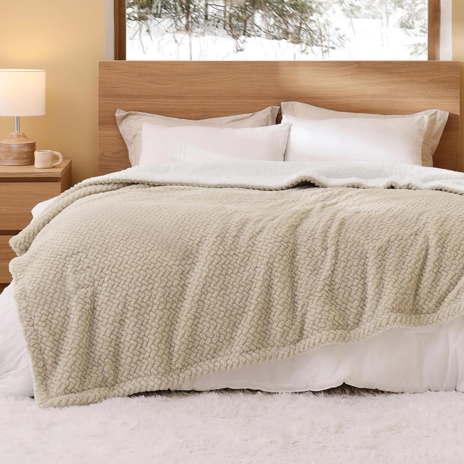 A beige Queen Sherpa Fleece Blanket with a textured pattern, draped over a bed featuring a wooden headboard. The setting has neutral tones, including pillows and a soft, white rug on the floor.
