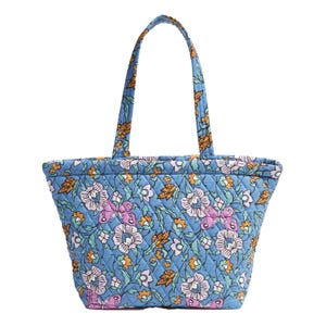 A quilted fabric tote bag with a vibrant blue background, featuring a floral and butterfly pattern in shades of pink, white, yellow, and green. It has two shoulder straps for easy carrying.