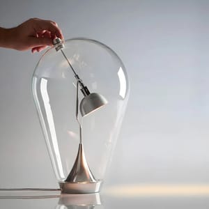 A sleek table lamp with a magnetic mid-air switch mechanism is encased in a large light bulb-shaped glass shell, creating an illusion of a floating switch.