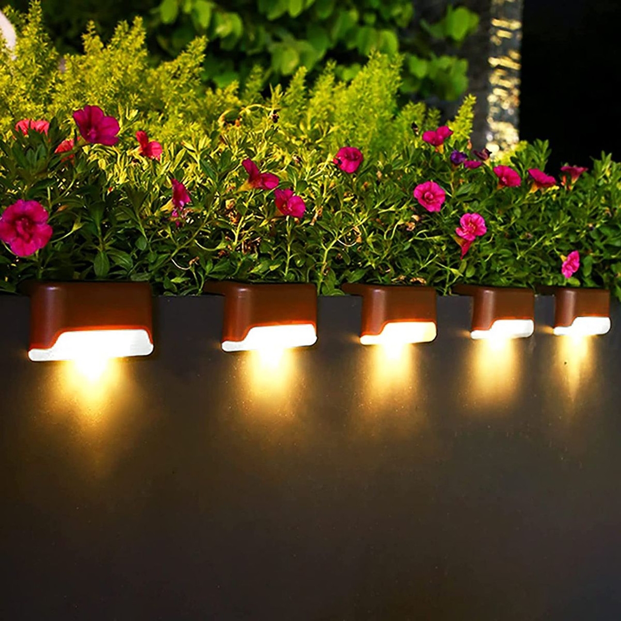 8pk Solar LED Pathway Lights feature sleek, compact brown housings with warm white light illuminating below, enhancing garden edges with small pink flowers above. Ideal for garden pathways or outdoor decoration.