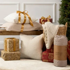 Cozy scene with decorative pillows, a knit blanket in a basket, wrapped gifts with gold ribbons, and a quilt set, all set beside a Christmas tree on a light rug.