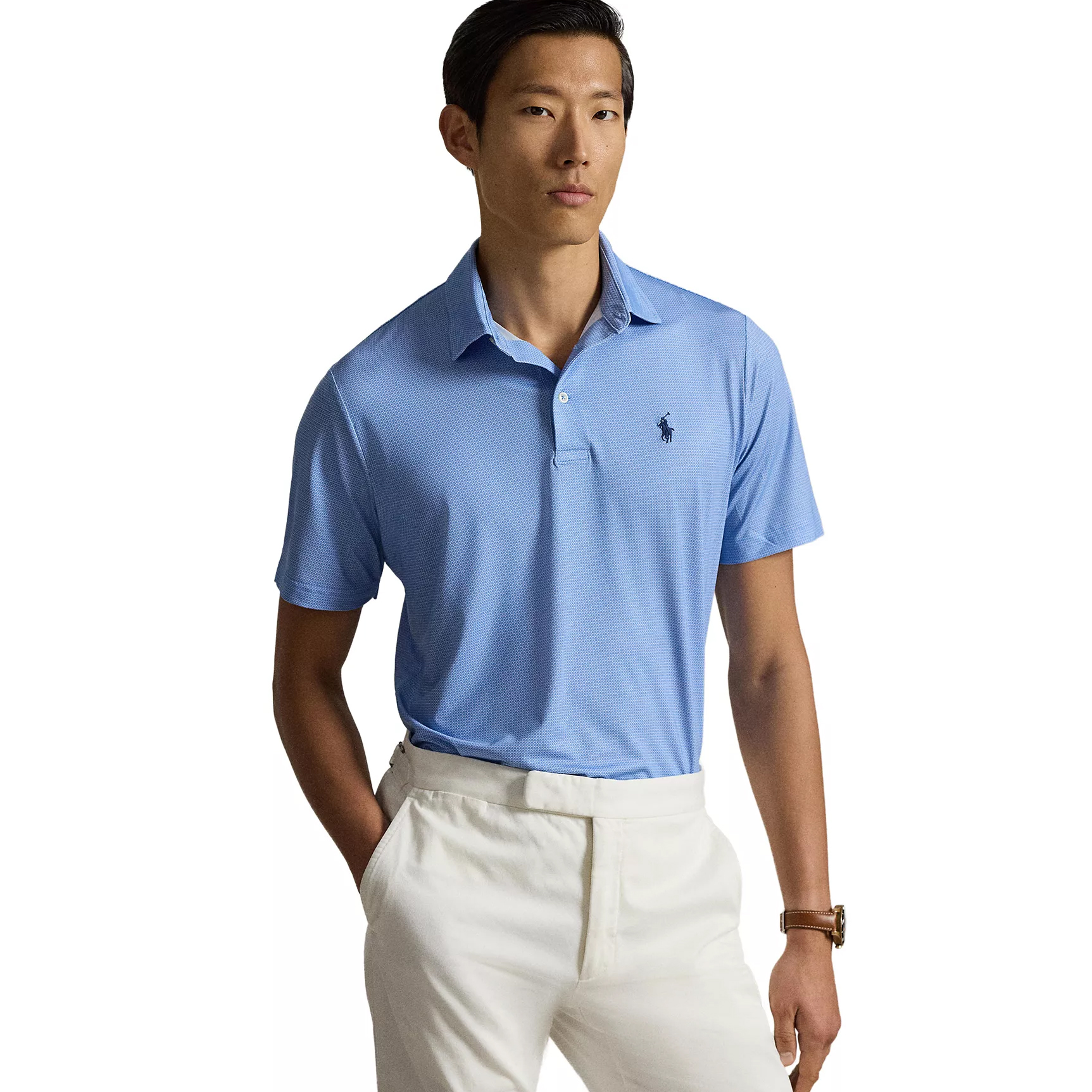 A man models a light blue polo shirt with a small dark logo on the chest, paired with white pants and a watch on his wrist.