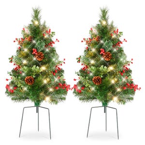 Two identical artificial Christmas trees decorated with red berries, pine cones, and warm white lights, each mounted on a simple metal stand.