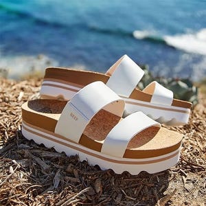 A pair of white strappy platform sandals by the sea.