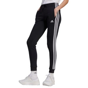 Adidas Women's Essentials Pants are black joggers featuring the iconic three white stripes down the sides, an elastic waistband with a drawstring, the Adidas logo on the thigh, and ribbed cuffs, paired with white sneakers and socks.