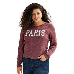 A woman wears a maroon long-sleeve thermal top with the word \“PARIS\“ printed in white across the chest, paired with blue jeans.