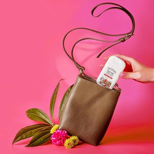 A brown leather crossbody bag with a strap, placed on a pink background, holds a hand pulling out a white bottle labeled \“Love Beauty and Planet,\“ surrounded by green leaves and colorful flowers.