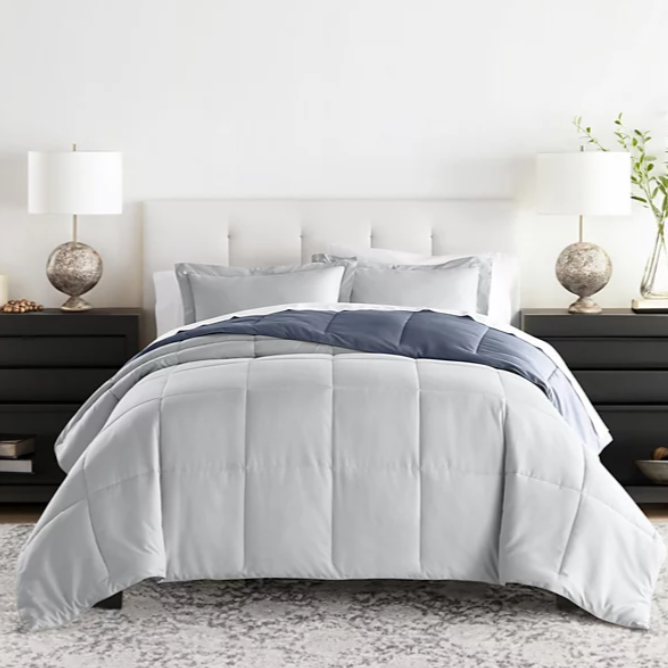 A neatly arranged bed with a tufted white headboard, light gray comforter, and dark blue accent blanket, accompanied by two black nightstands with identical lamps and decor, on a textured gray rug.