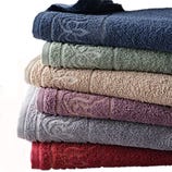 A stack of six folded, colorful towels featuring decorative patterns on their borders.