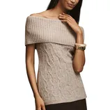 A woman is wearing an off-the-shoulder beige ribbed and cable-knit sweater, accessorized with white and gold bangles on her wrist.