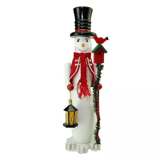 A snowman figurine with a black top hat, red scarf, and two beaded garlands holds a lantern in one hand and a stick with a red birdhouse and cardinal in the other.