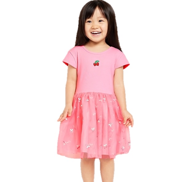 A young girl is wearing a pink dress with a T-shirt style top featuring a cherry design and a tulle skirt adorned with small white bows.