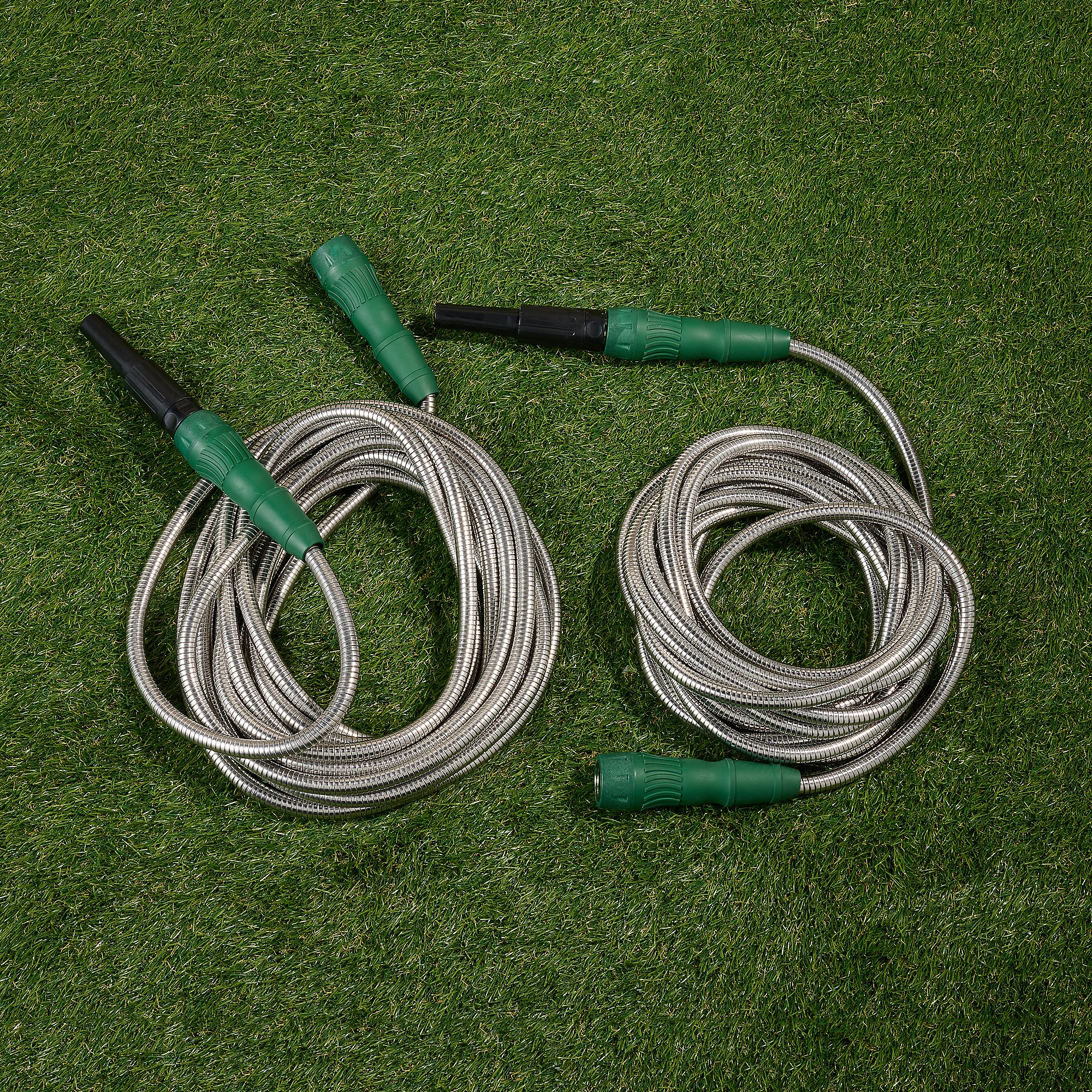 2pk Expanding Metal Hoses feature a durable stainless steel construction with green plastic connectors and black nozzles, neatly coiled on green grass.